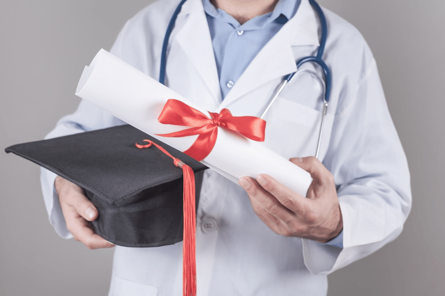 Doctor in white coat holding a graduation cap and diploma tied with a red ribbon, symbolizing medical school graduation.