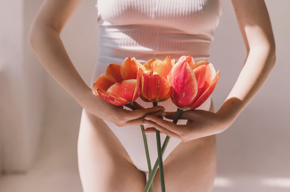 Young woman holds tulip near bikini zone representing genital health.