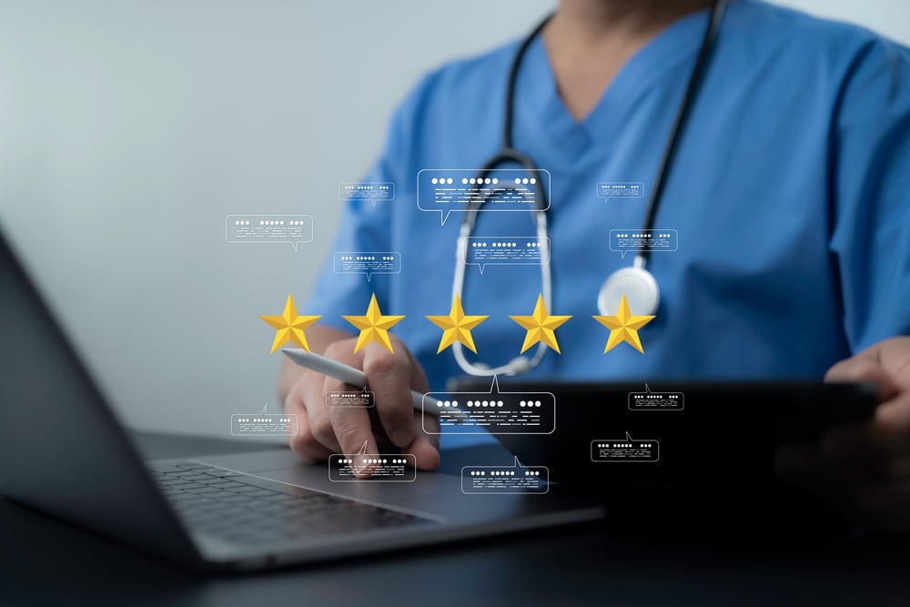 Doctor using a laptop and stylus surrounded by five star feedback and digital comment icons.