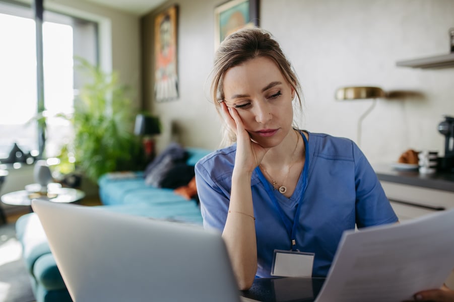 Nurse paying bills online, sitting in living room, working on notebook.
