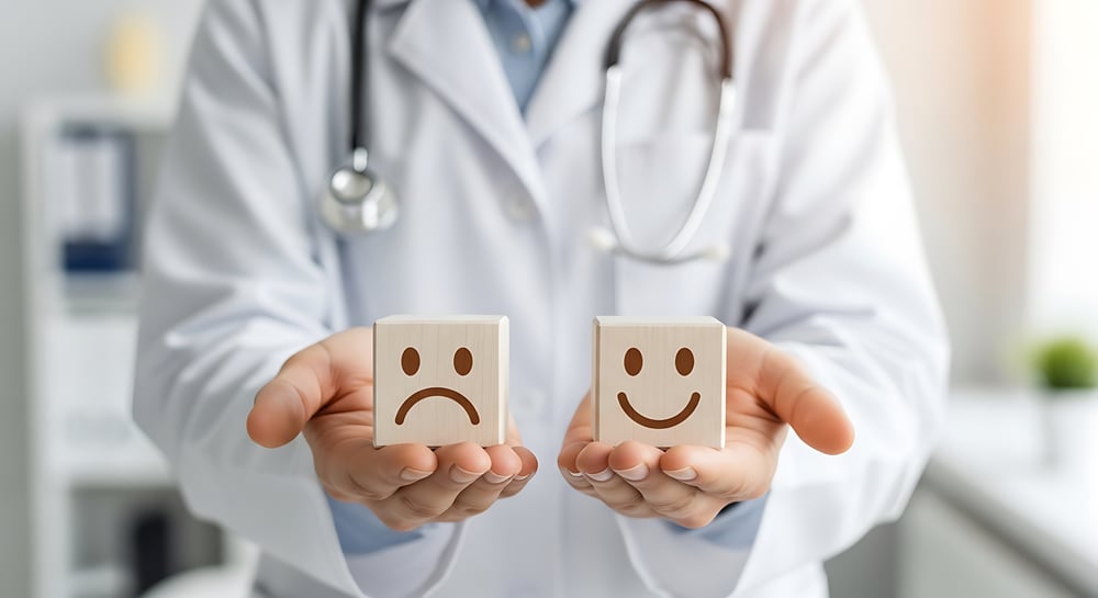 A man in a doctor's coat holding one sad and one smily face wooden cube - one in each hand.