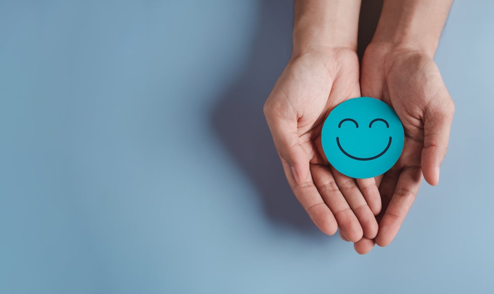 A round smily face held in palms on a blue background.